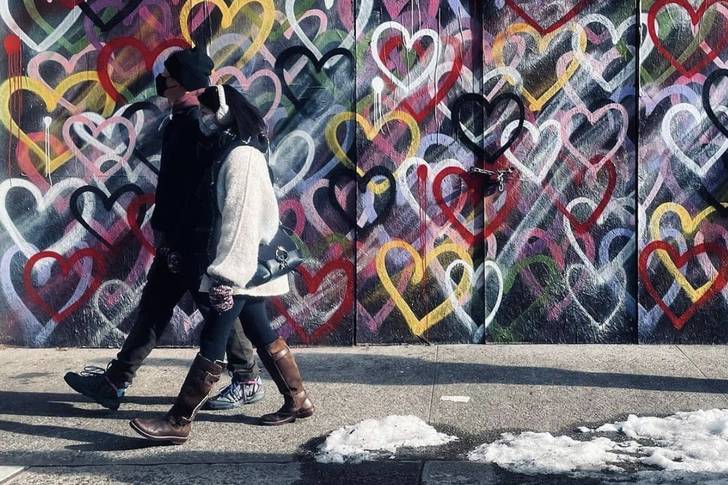 Two people walk past a wall in NYC painted with hearts.